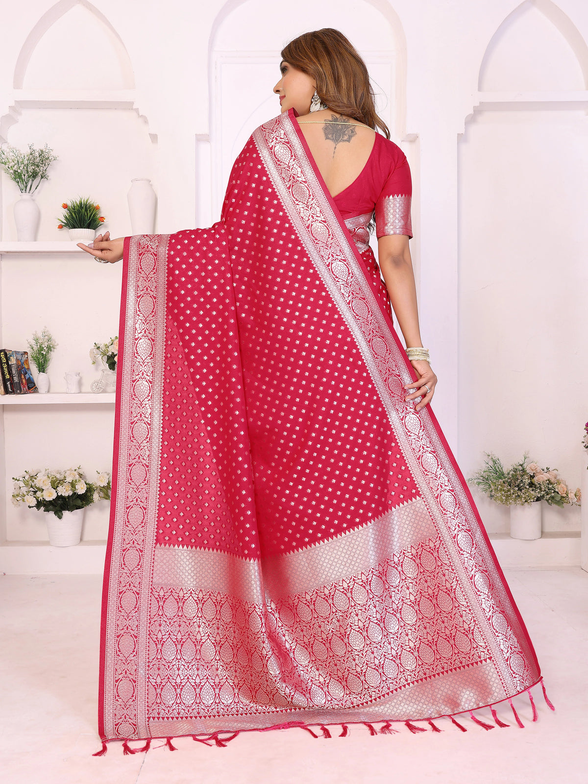 Woman wearing a red saree with white patterns in a white room.