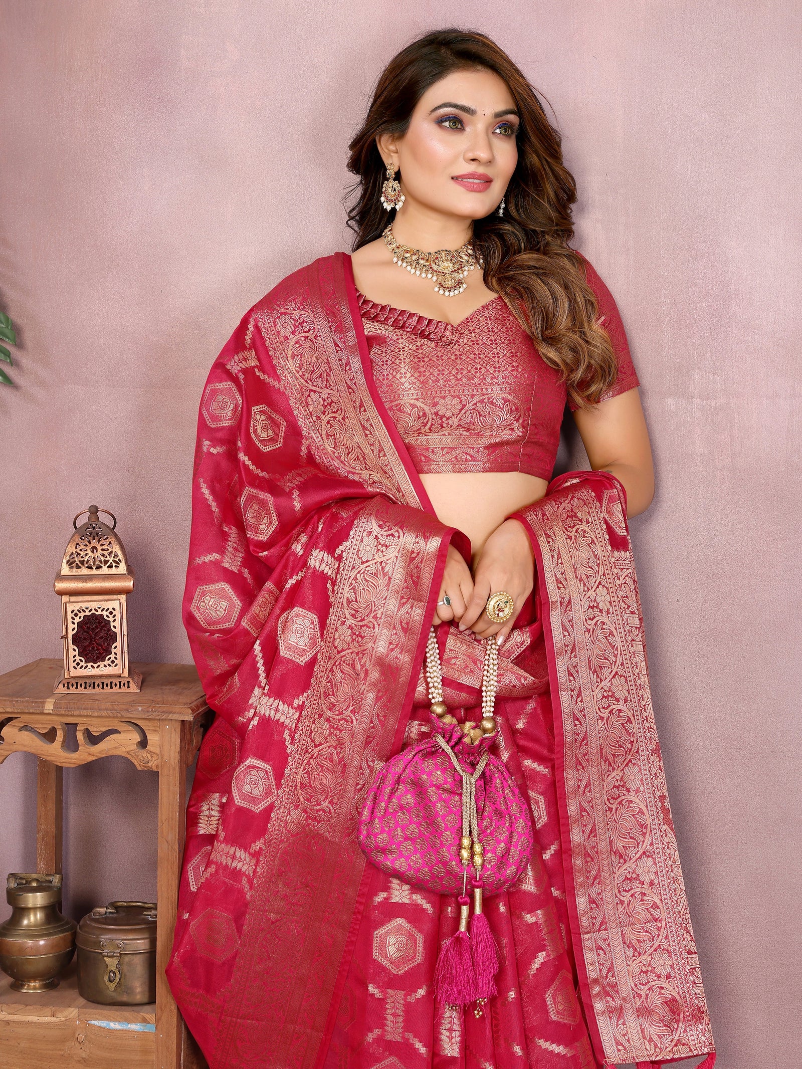 Woman wearing a red saree with white patterns, holding a matching handbag, against a pink background.