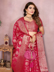 Woman wearing a red saree with white patterns, holding a matching handbag, against a pink background.