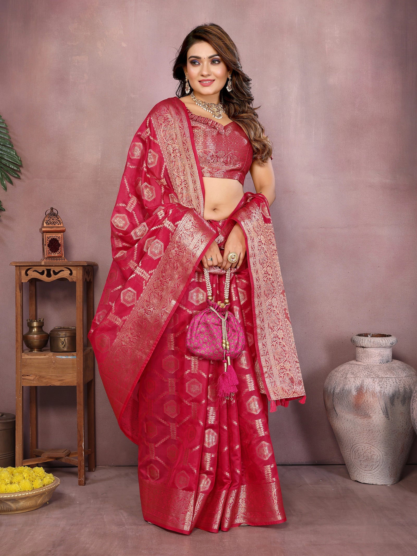 Woman in a red saree with gold patterns standing against a neutral background
