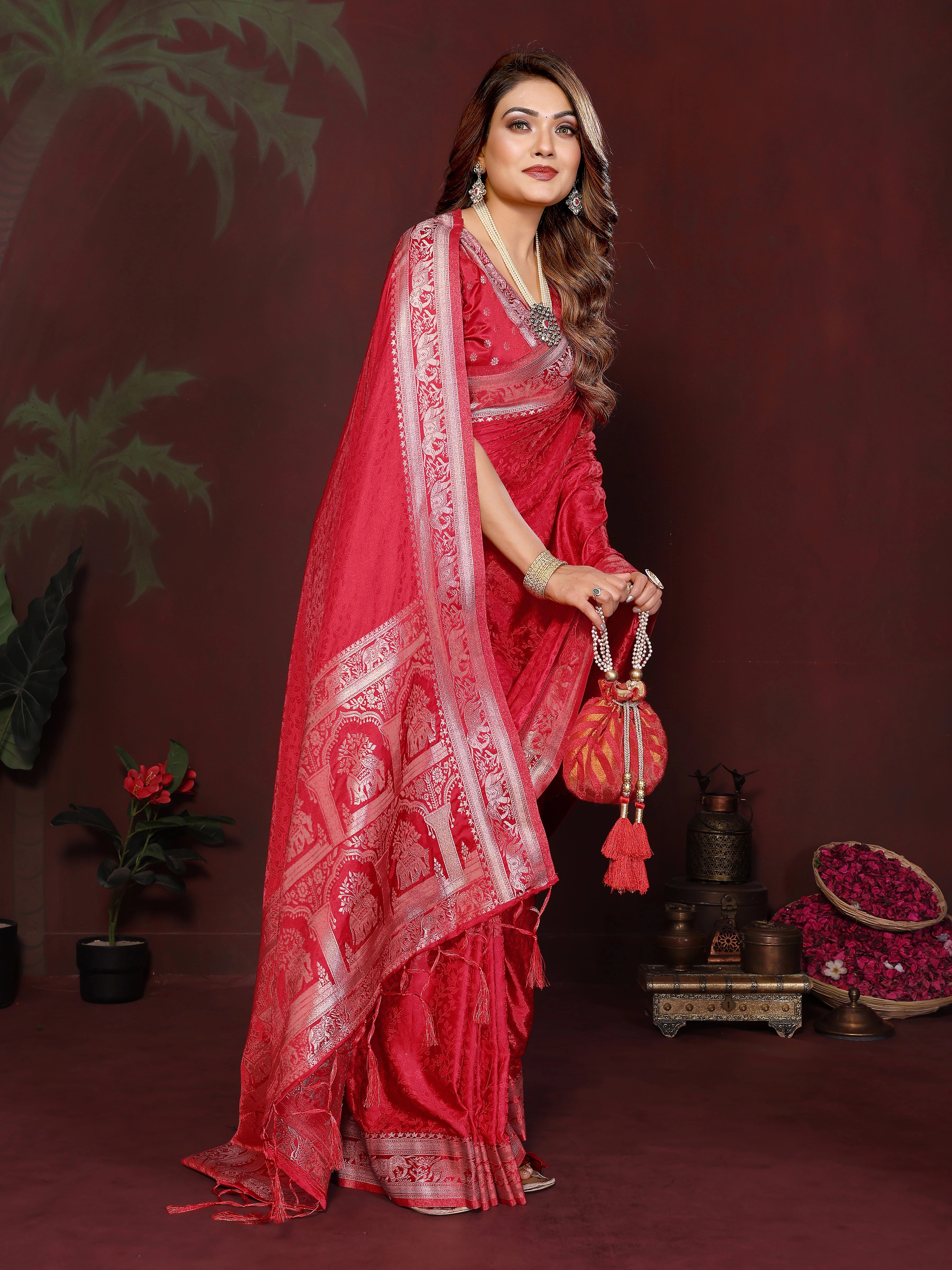 Woman in a red saree with white patterns holding a matching bag against a dark background