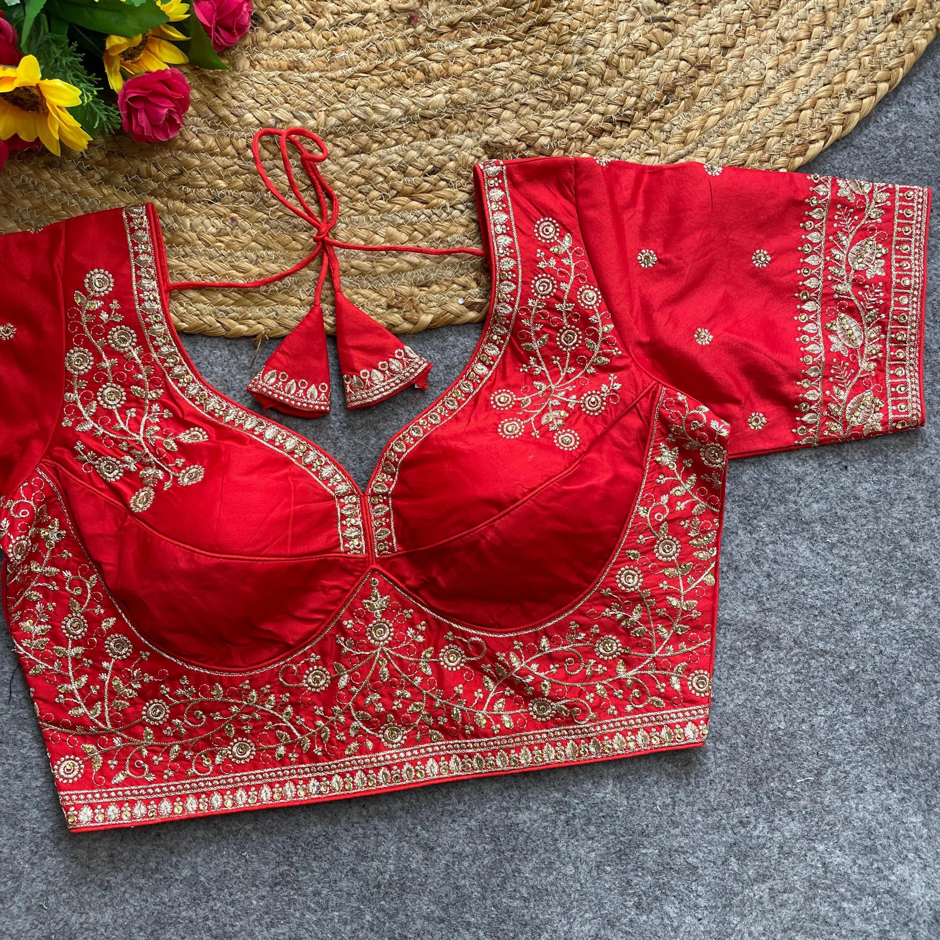 Red embroidered blouse with gold details on a gray surface, with flowers in the background.