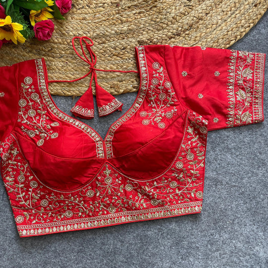 Red embroidered blouse with gold details on a gray surface, with flowers in the background.