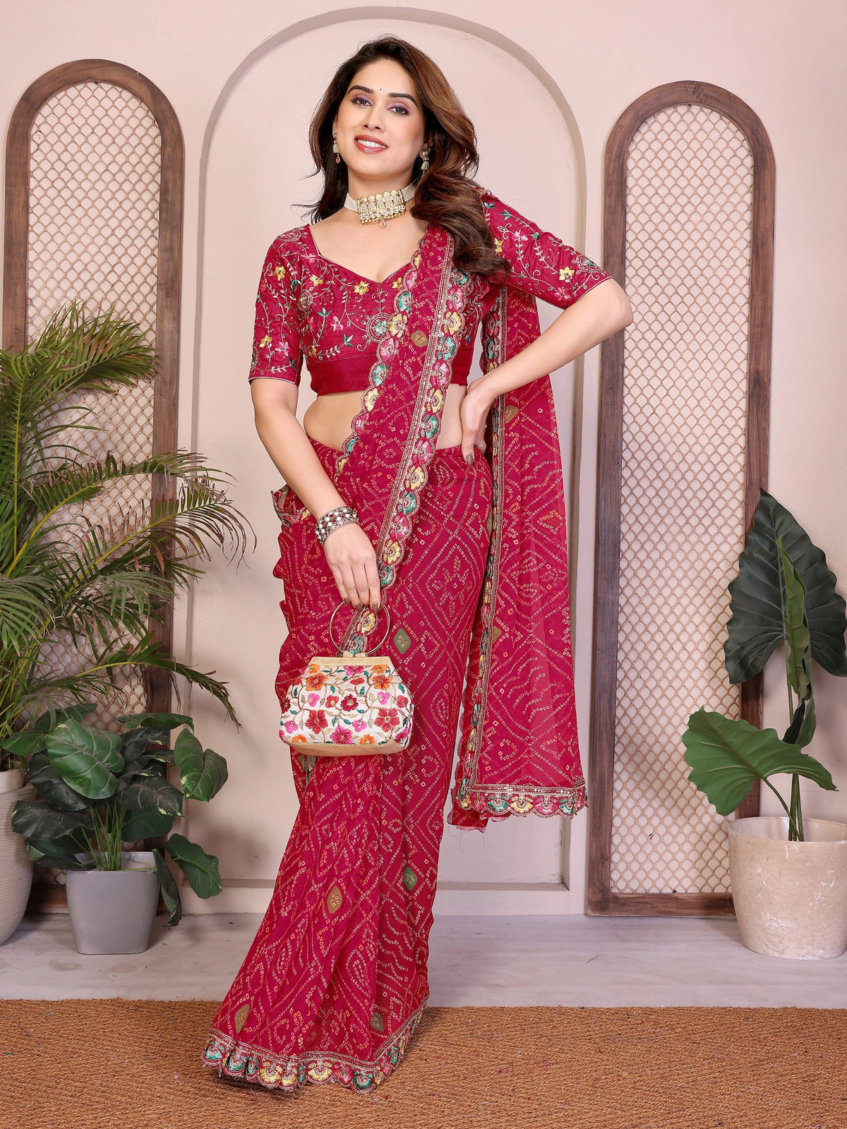 Woman in a red saree with floral patterns standing indoors with plants in the background