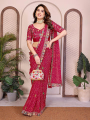 Woman in a red saree with floral patterns standing indoors with plants in the background