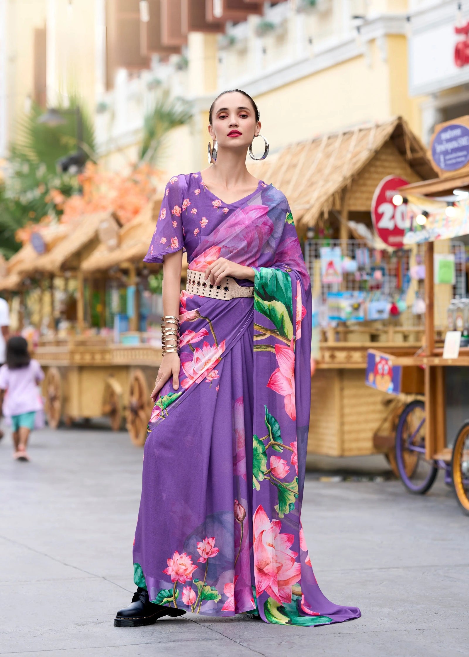 Woman in a vibrant purple saree with floral patterns walking on a street.