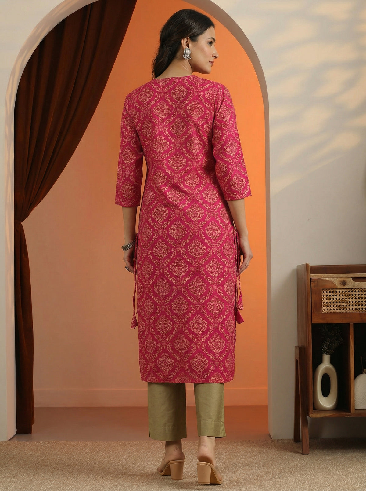 Woman wearing a pink traditional outfit standing in a room with an orange wall.