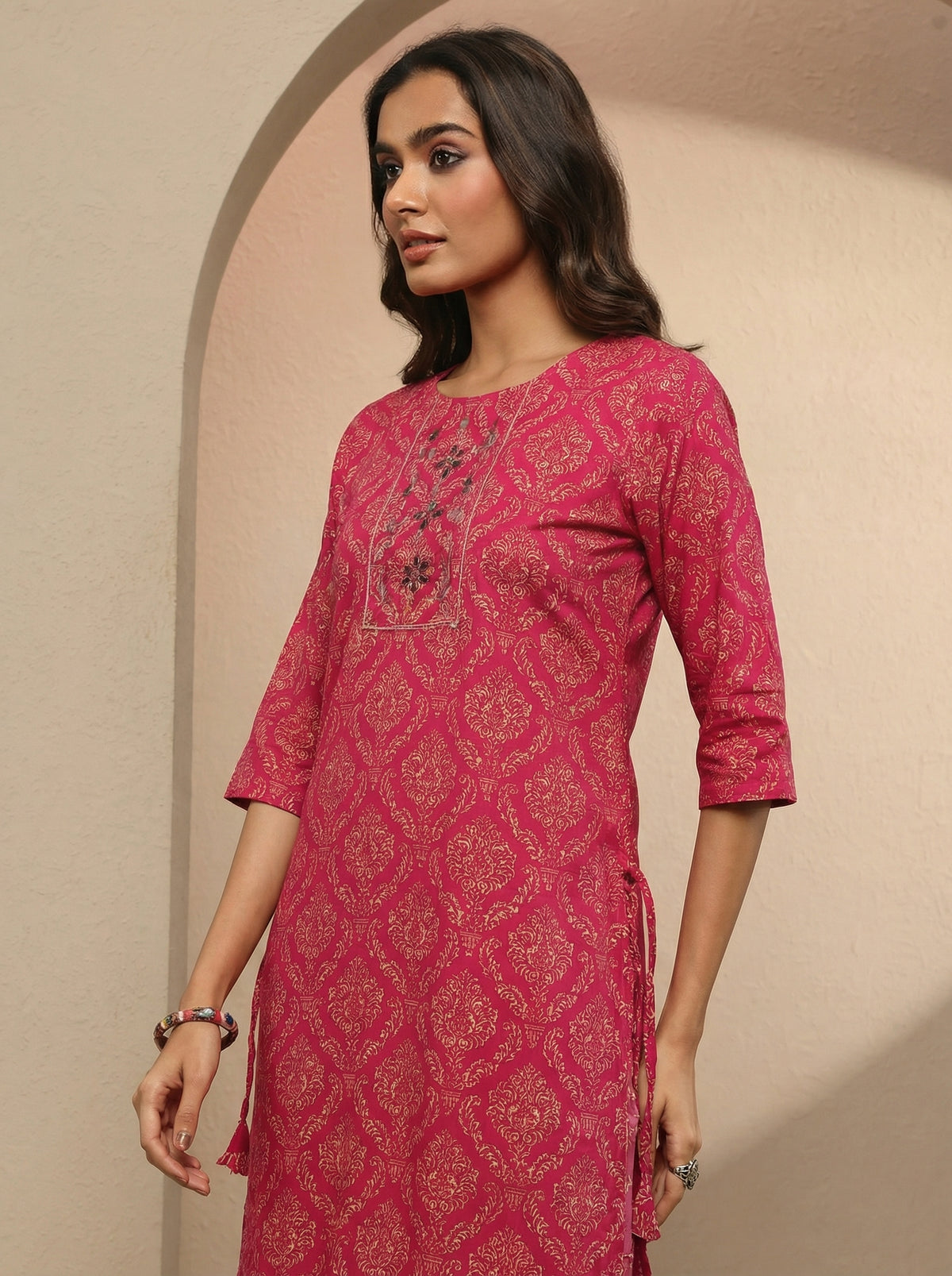 Woman wearing a pink patterned kurta against a beige background