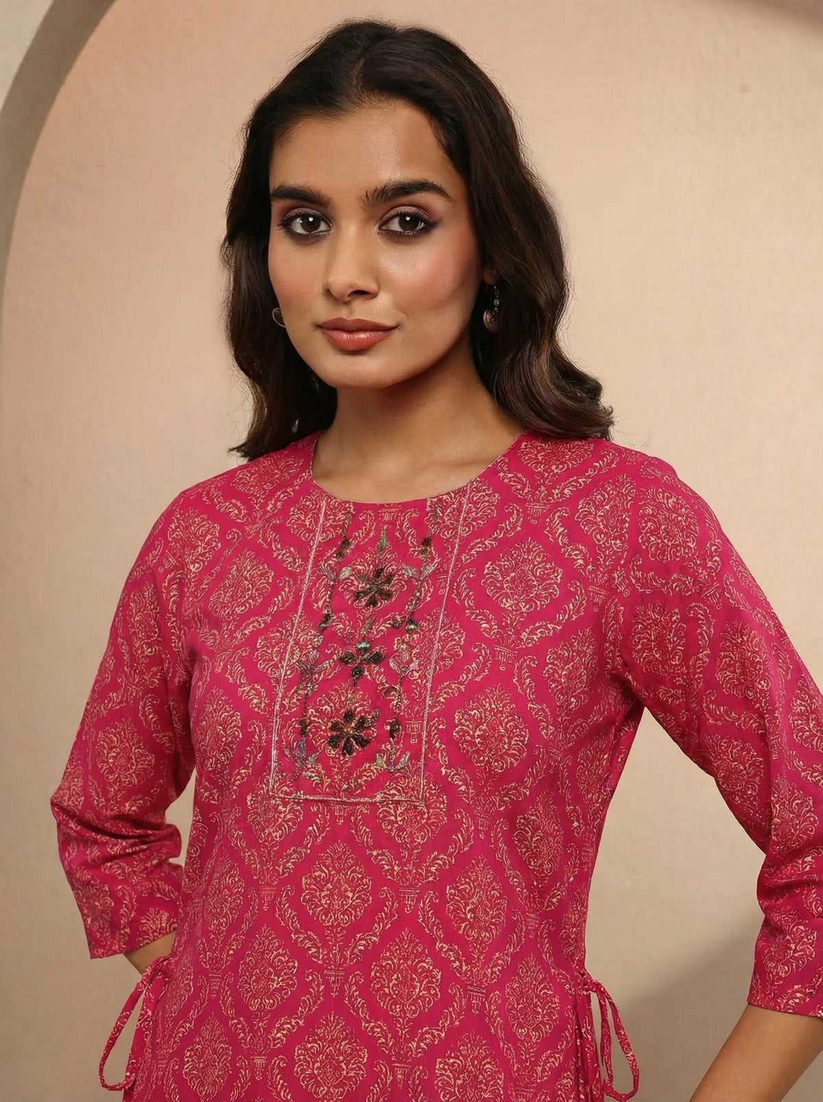 Woman wearing a pink embroidered traditional outfit against a beige background