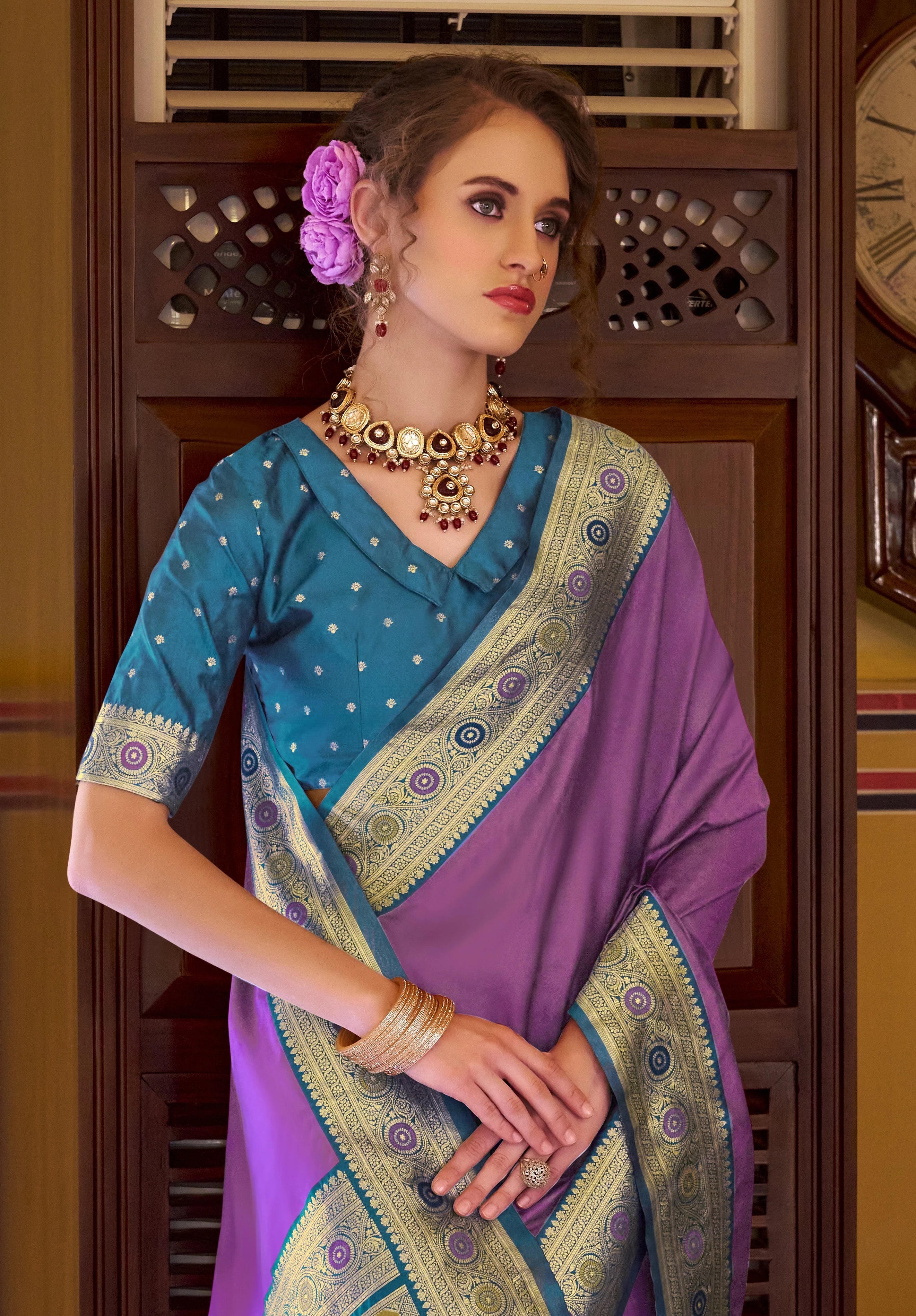 Woman wearing a traditional purple and blue saree with gold border indoors.