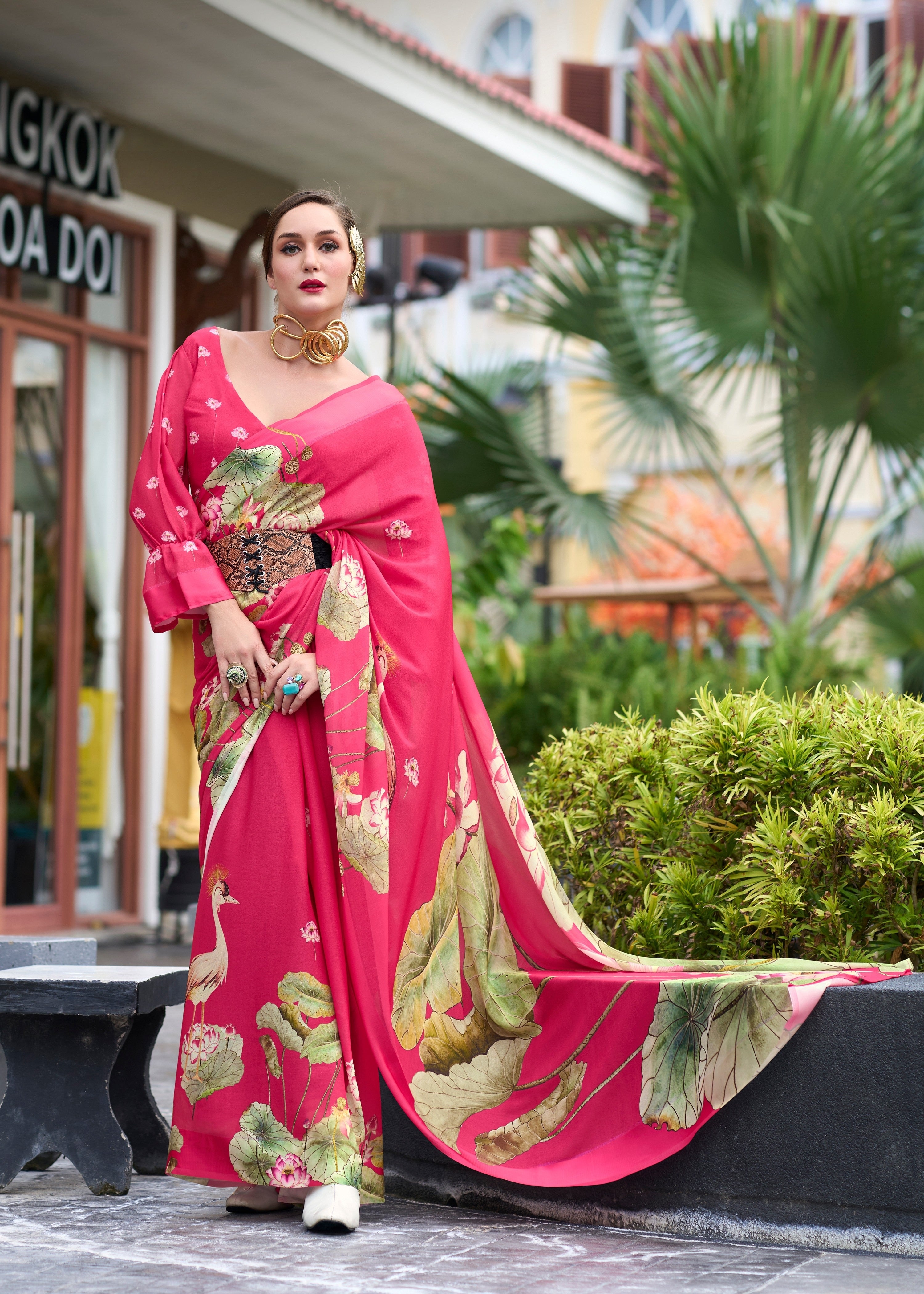 Woman in a pink saree with floral patterns standing outdoors.