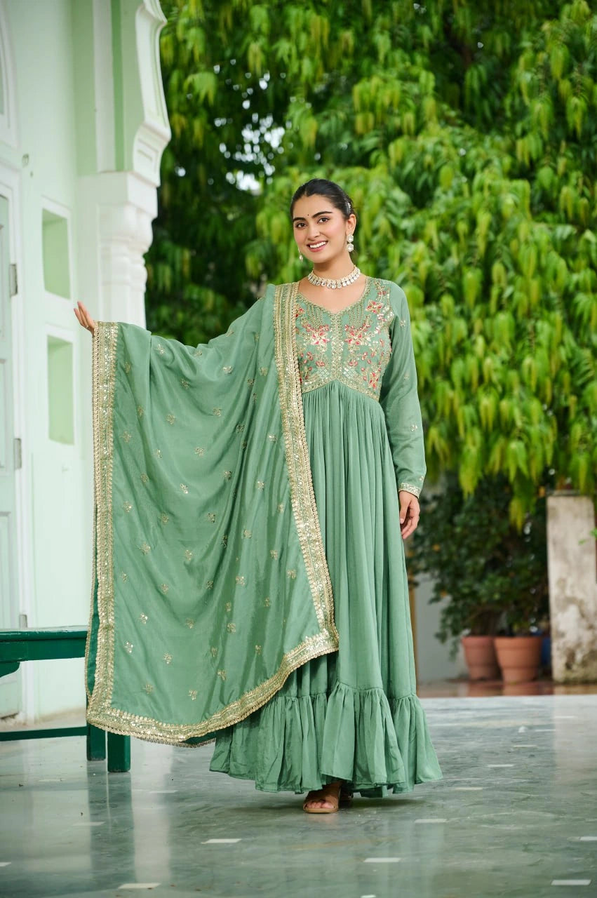 Woman in a green traditional outfit standing outdoors with greenery in the background