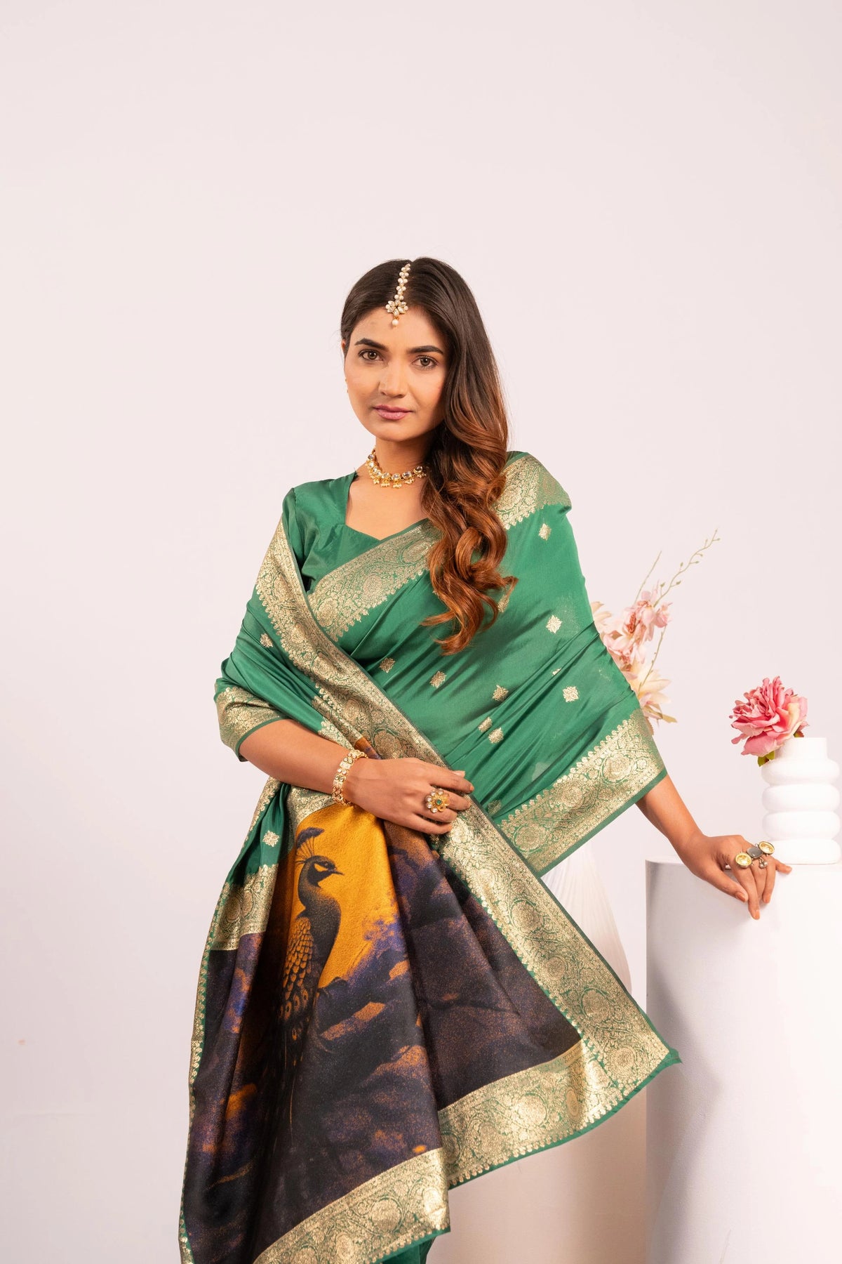 Woman wearing a green saree with a black and gold border, standing against a white background.