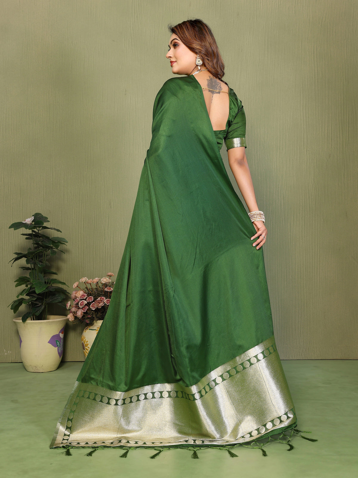 Woman wearing a green saree with a gold border against a green background