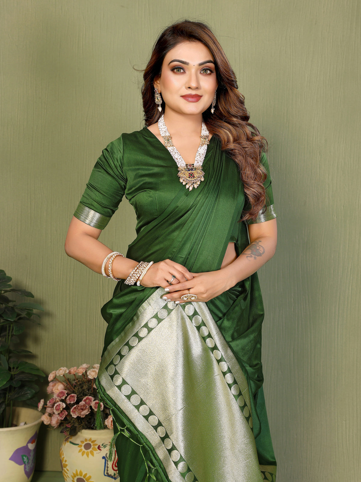 Woman wearing a green saree with a white border against a plain background