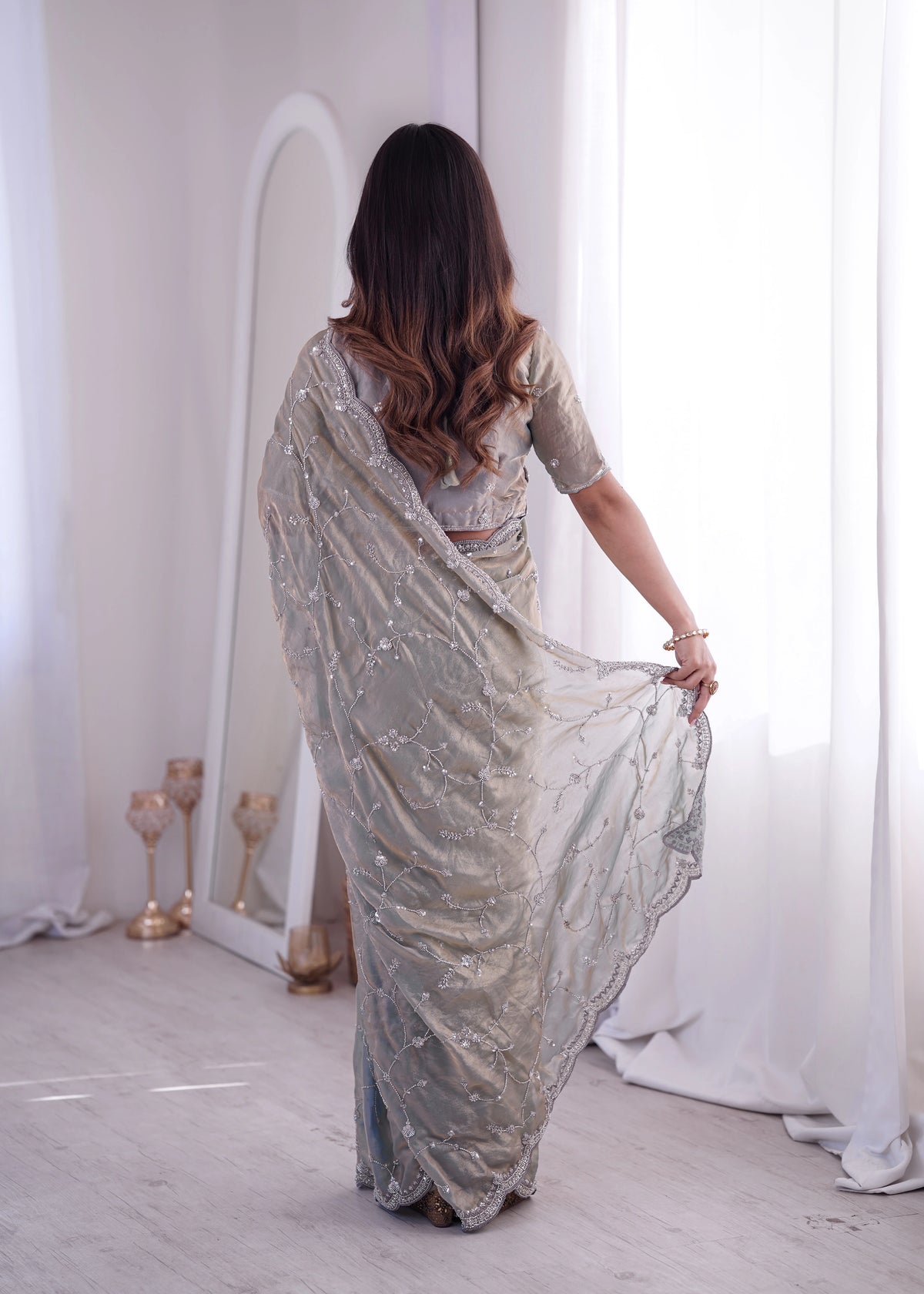 Woman wearing a silver saree in a minimalistic room with white curtains.