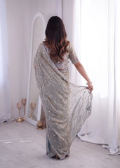 Woman wearing a silver saree in a minimalistic room with white curtains.