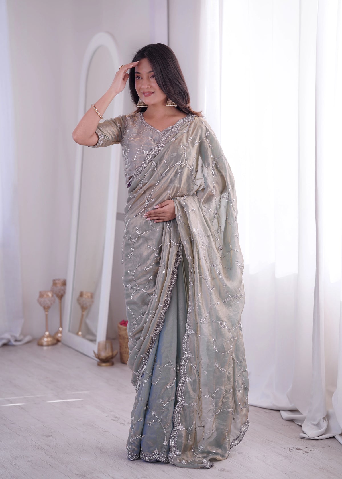 Woman wearing a silver saree with a mirror and white curtains in the background