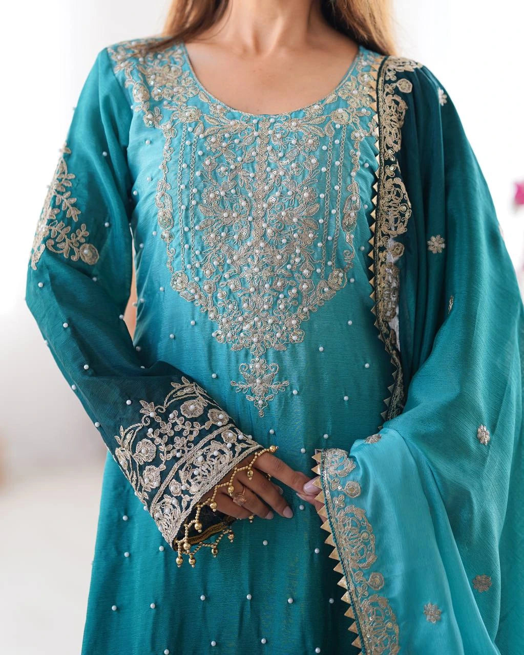Teal embroidered traditional outfit with gold detailing on a white background
