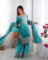 Woman wearing a turquoise embroidered traditional outfit with a white curtain background