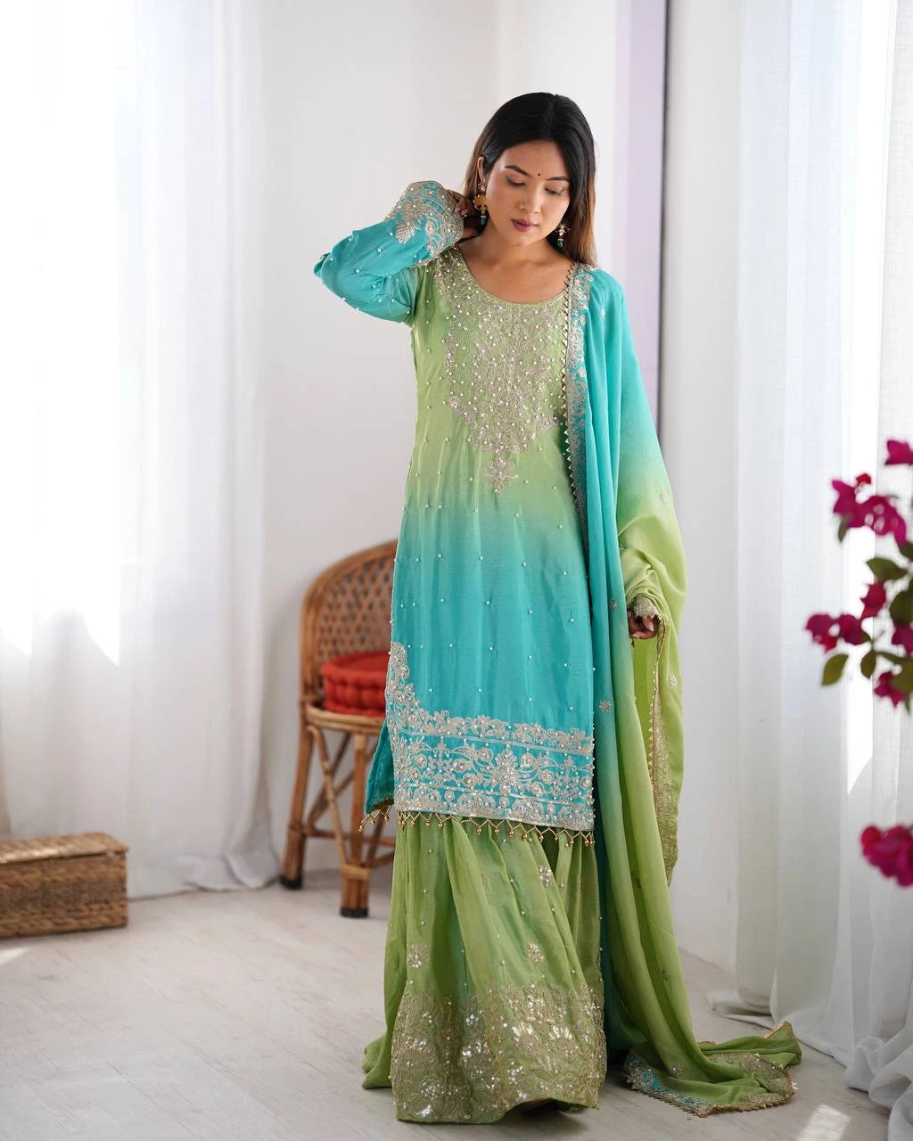 Woman wearing a green and blue traditional outfit with a white curtain background