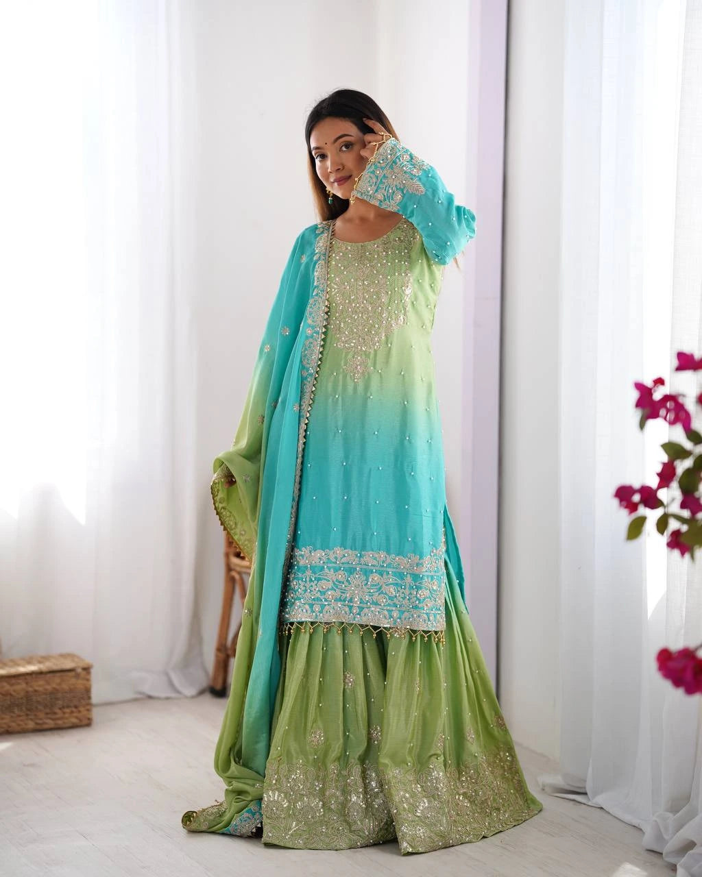Woman wearing a green and blue traditional outfit with a white curtain background