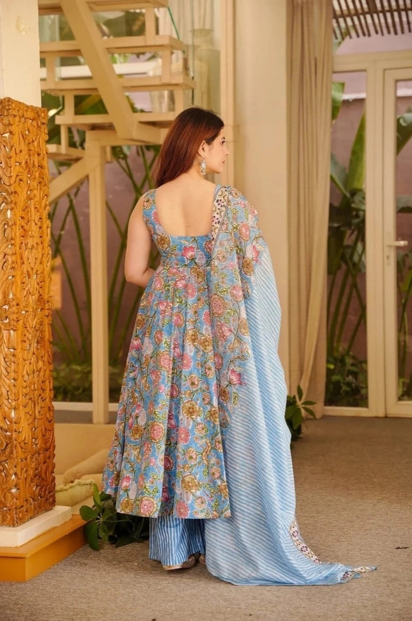 Woman in a floral dress and blue dupatta standing in a room with decorative elements.