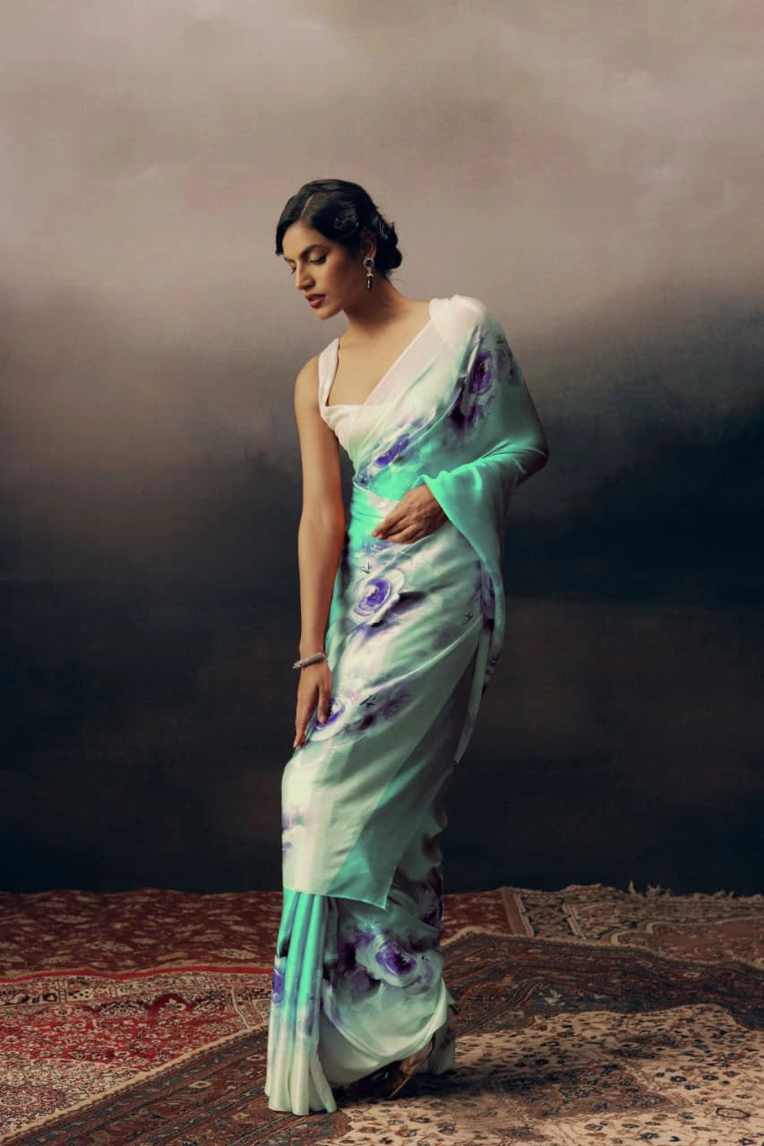 Woman wearing a light green saree with floral patterns on a textured floor.