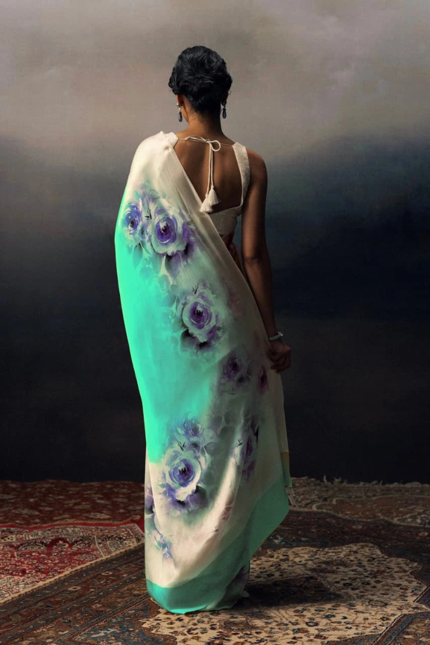 Woman wearing a teal saree with floral patterns on a dark background