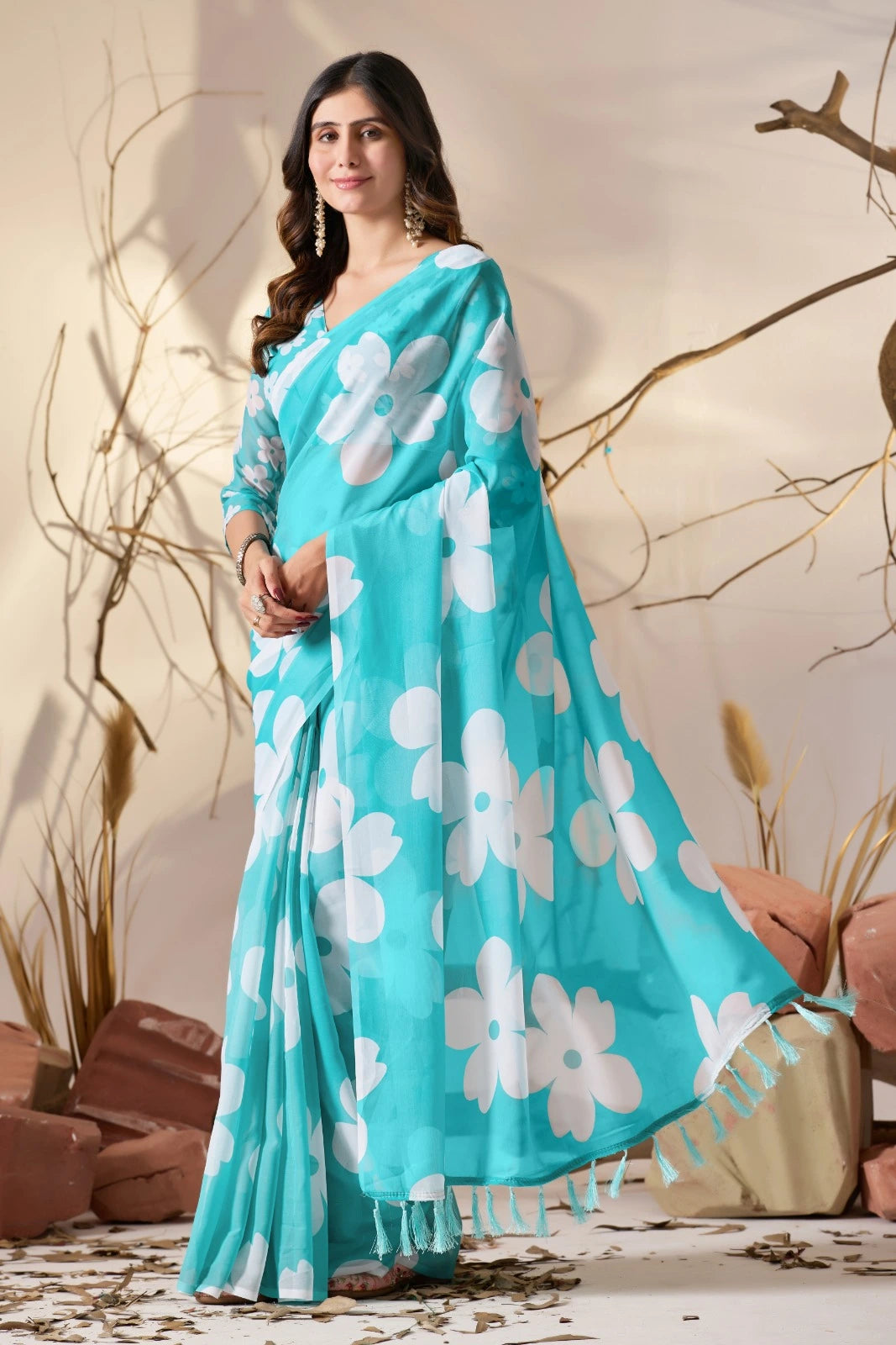Woman wearing a turquoise saree with white floral patterns against a neutral background