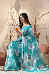 Woman in a blue floral saree reading a book in a cozy indoor setting.