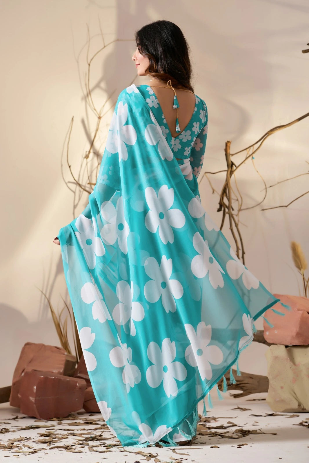 Woman wearing a turquoise dress with white floral patterns, standing against a neutral background.
