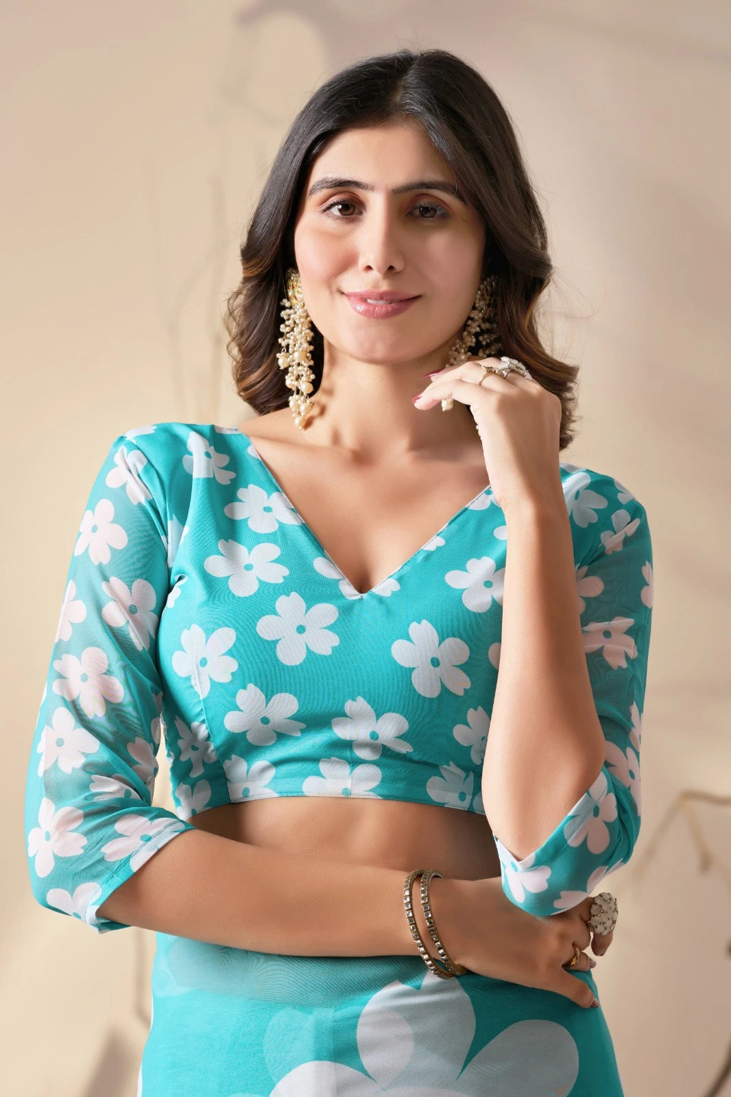 Woman wearing a turquoise blouse with white floral patterns on a neutral background