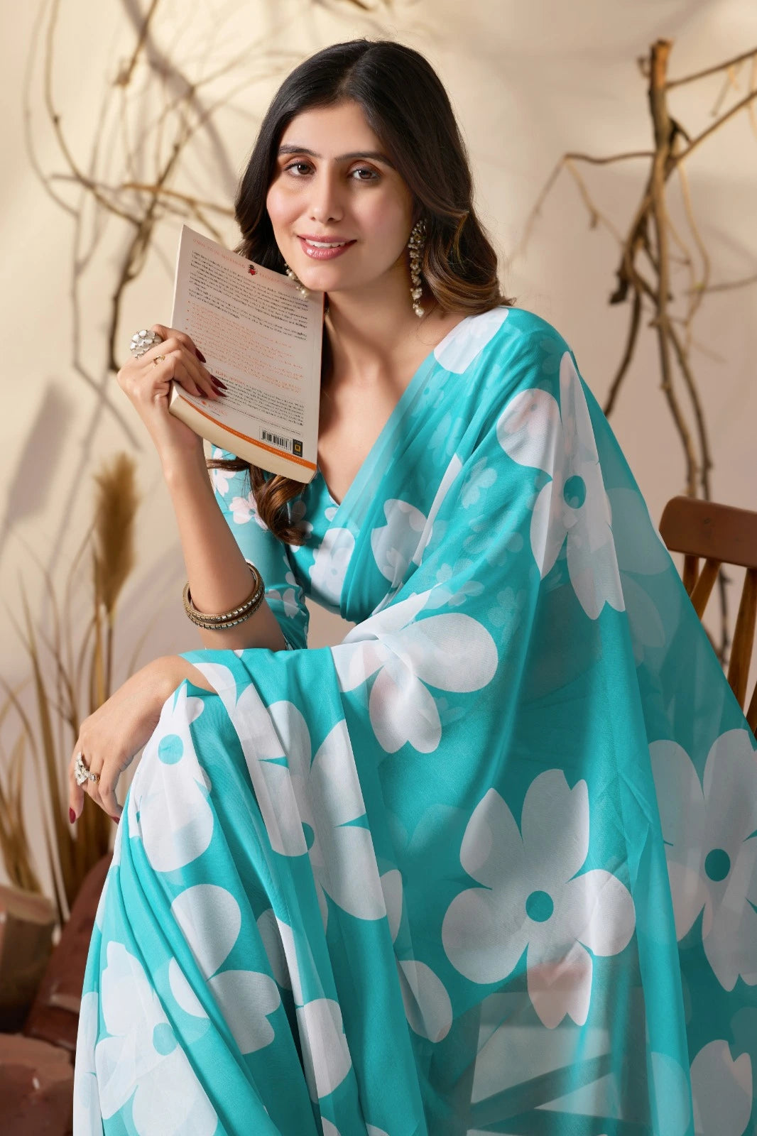 Woman wearing a turquoise saree with white floral patterns, holding a book.