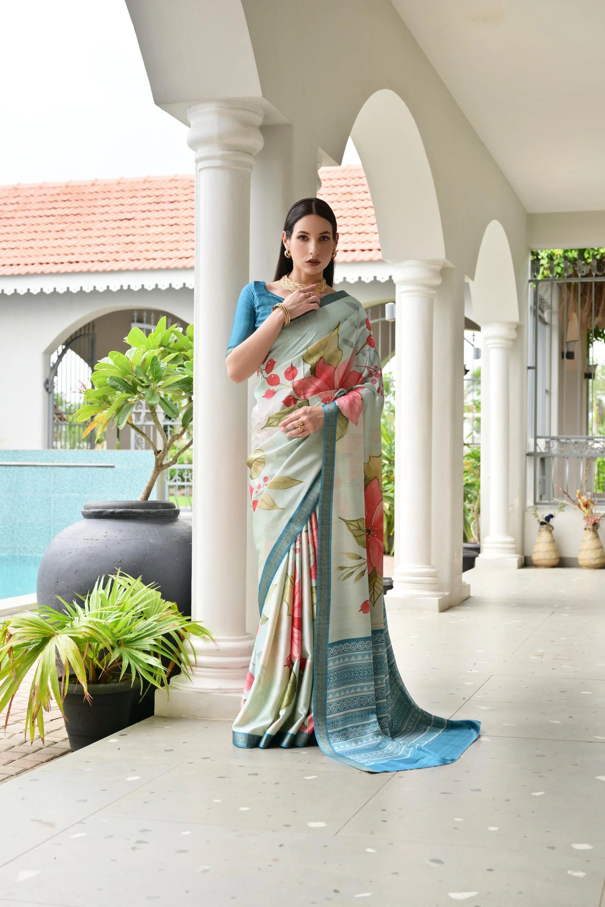 Woman wearing a floral saree in an outdoor setting with columns and plants.