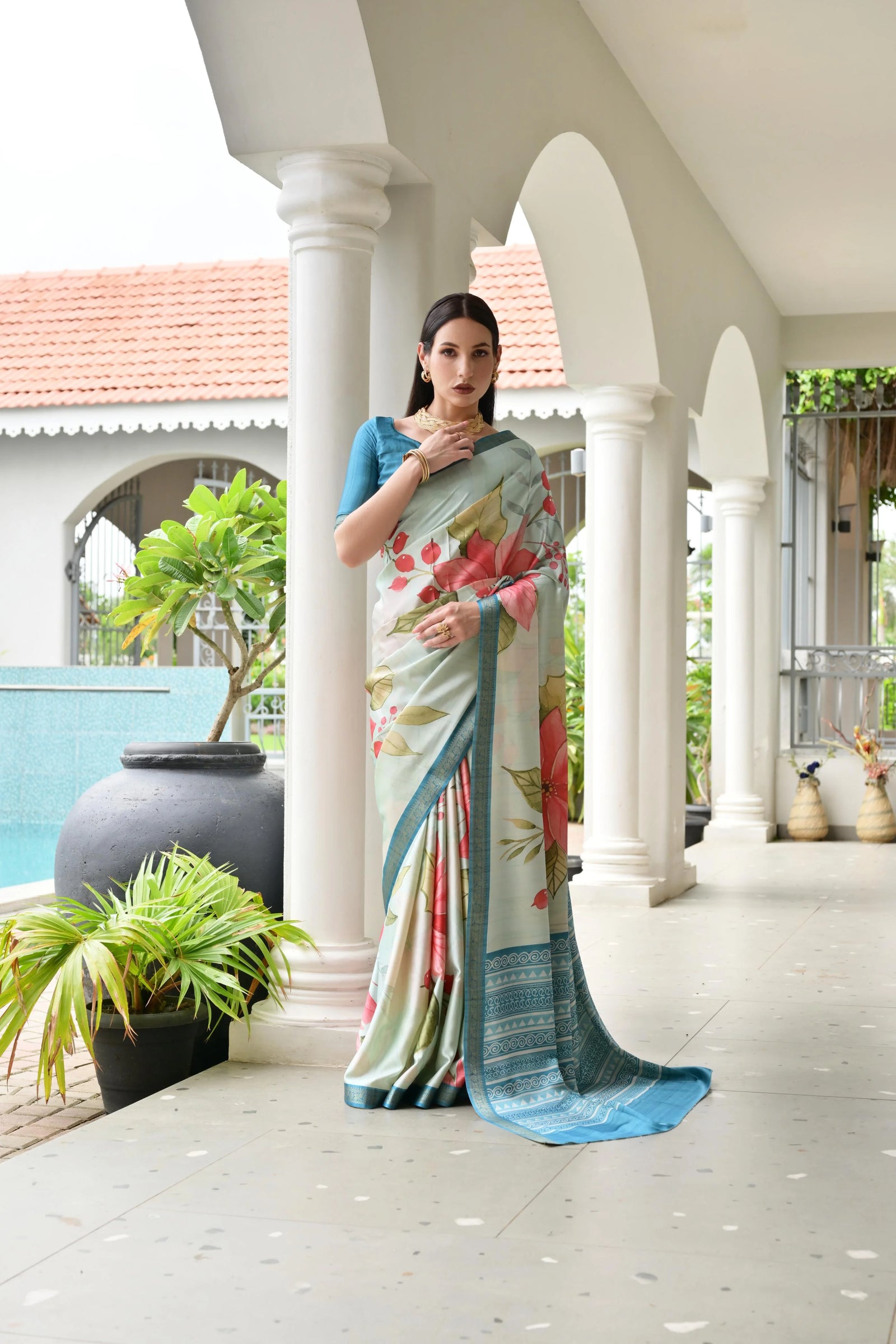 Woman wearing a floral saree in an outdoor setting with columns and plants.