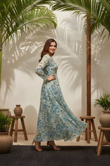 Woman in a floral dress standing in a room with plants and wooden stools.
