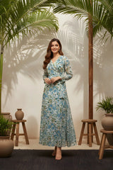 Woman in a floral dress standing in a room with plants and wooden stools.