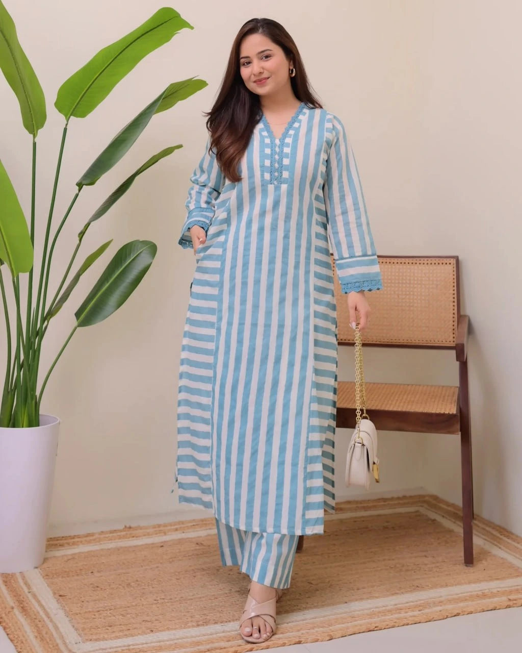 Woman wearing a blue and white striped outfit standing in a room with a plant and chair.