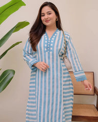 Woman wearing a blue and white striped dress with a plant and chair in the background