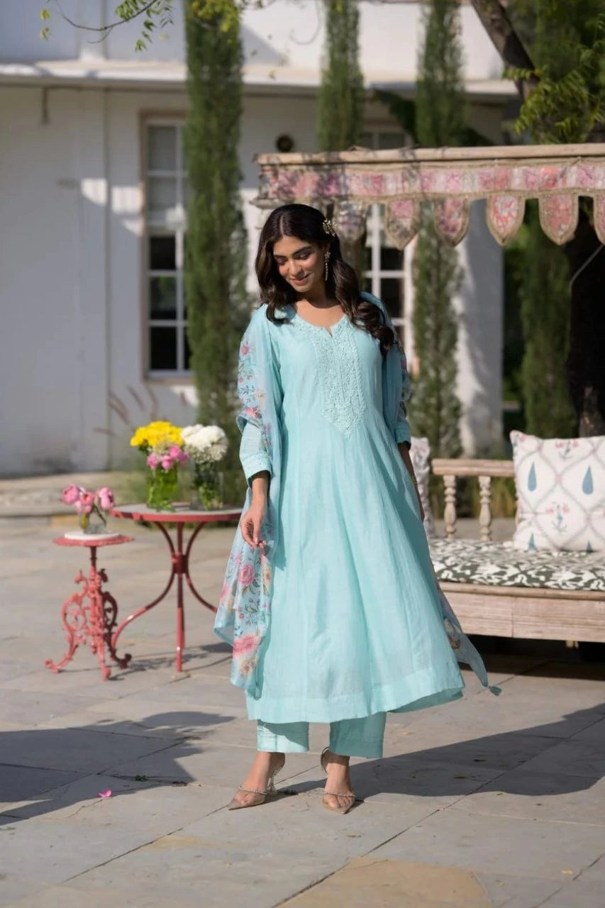 Woman in a light blue traditional outfit standing outdoors with a decorative background