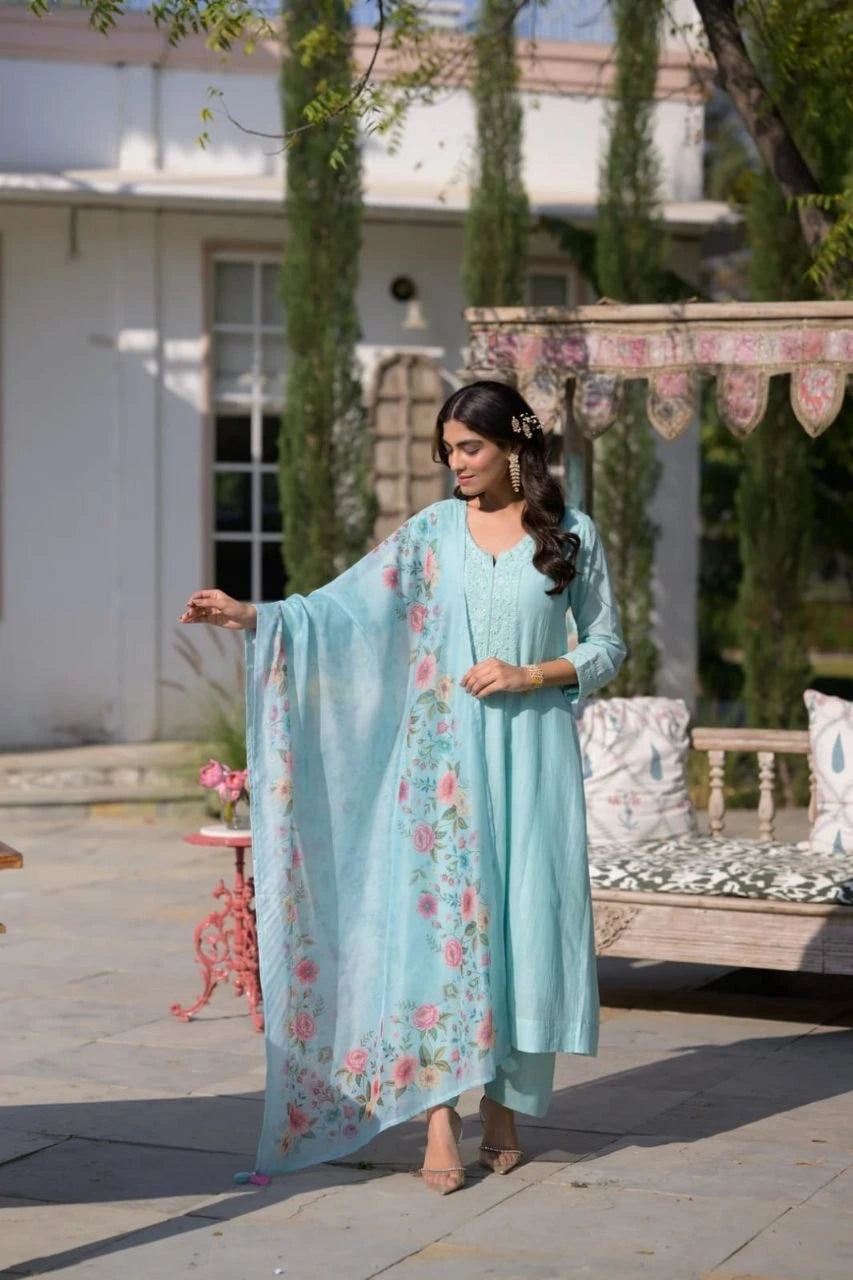 Woman in a light blue traditional outfit with floral patterns standing outdoors.