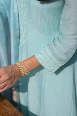 Light blue shirt with rolled-up sleeves and a bracelet worn on a wrist.