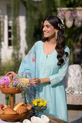 Woman in a light blue traditional outfit standing next to a table with food and flowers.