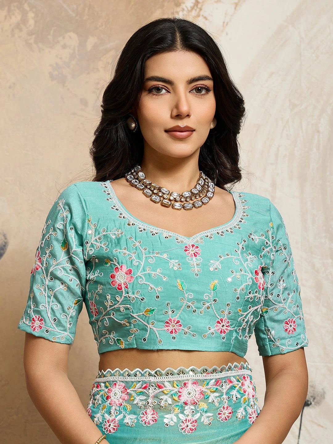 Woman wearing a teal embroidered blouse with a beige background