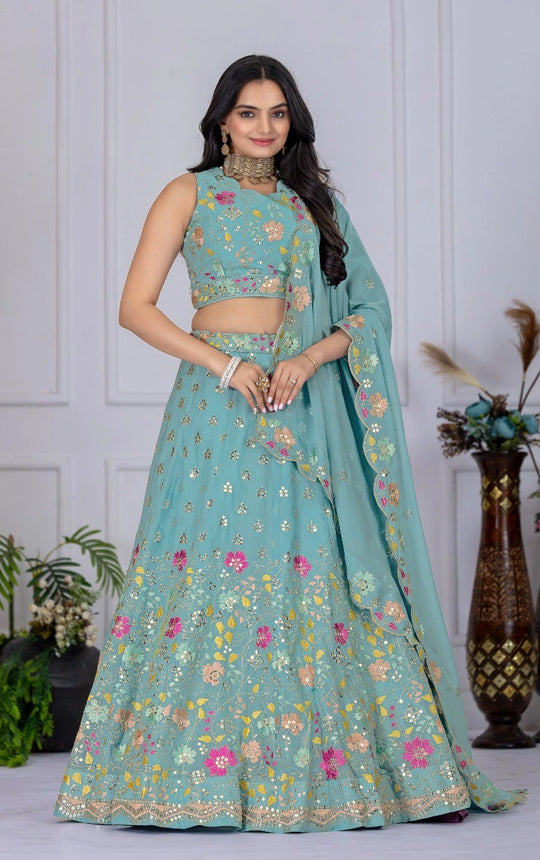 Woman wearing a light blue embroidered lehenga with a matching blouse against a white wall.