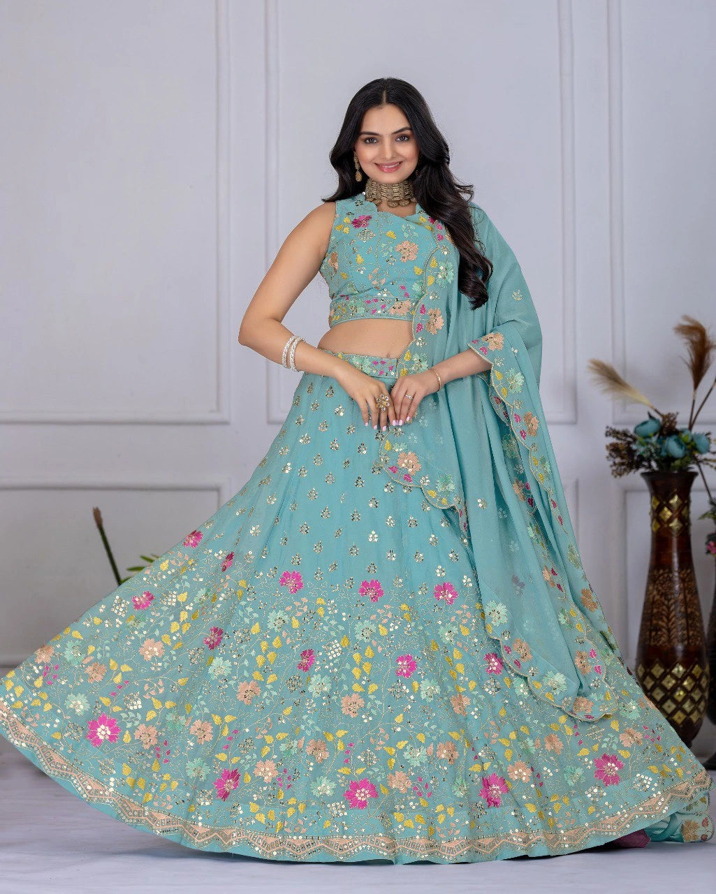 Woman wearing a teal floral lehenga with a matching blouse against a white wall.