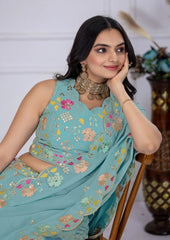 Woman wearing a light blue embroidered saree with floral patterns, sitting on a chair.