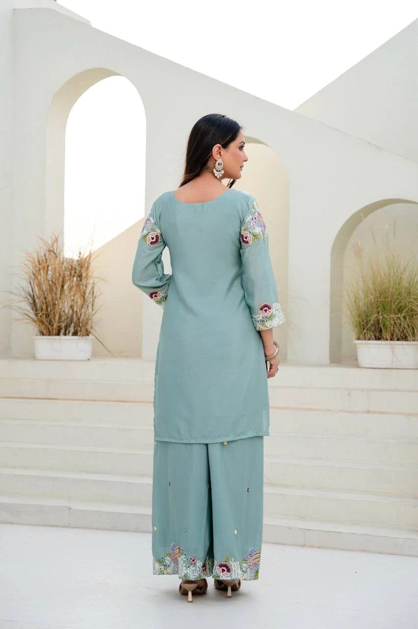 Woman wearing a light blue traditional outfit with floral embroidery in an architectural setting.