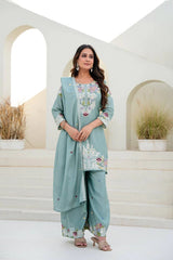 Woman wearing a light blue embroidered traditional outfit standing in a decorative setting.